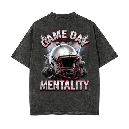 A dark gray acid-wash t-shirt shown from the back, featuring a graphic of a football helmet with smoke and the text 'GAME DAY MENTALITY' in white and red.