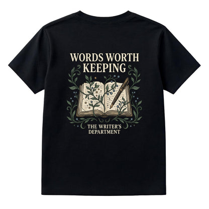 A black short-sleeve t-shirt shown from the back, featuring a graphic print of an open book with a quill and the text 'WORDS WORTH KEEPING' and 'THE WRITER'S DEPARTMENT' in cream and green.