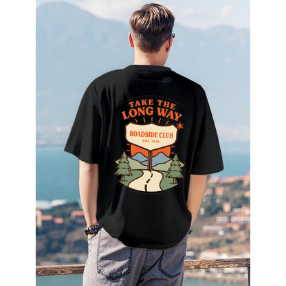 A man viewed from behind wearing a black graphic t-shirt with a retro-style 'Roadside Club' design on the back, set against a scenic coastal background.