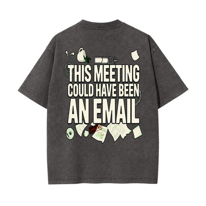 A dark gray washed t-shirt shown from the back, featuring a humorous graphic print that reads 'THIS MEETING COULD HAVE BEEN AN EMAIL' in bold white letters, surrounded by small illustrations of office items like a headset, coffee mug, and papers.