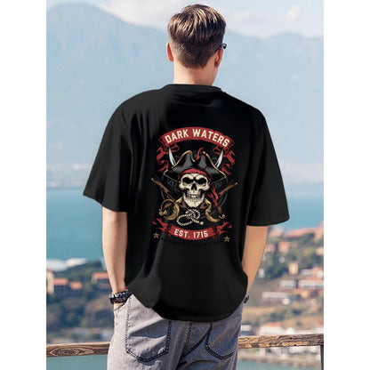 A man viewed from behind wearing a black t-shirt with a large pirate-themed graphic on the back, standing outdoors with a scenic coastal background.