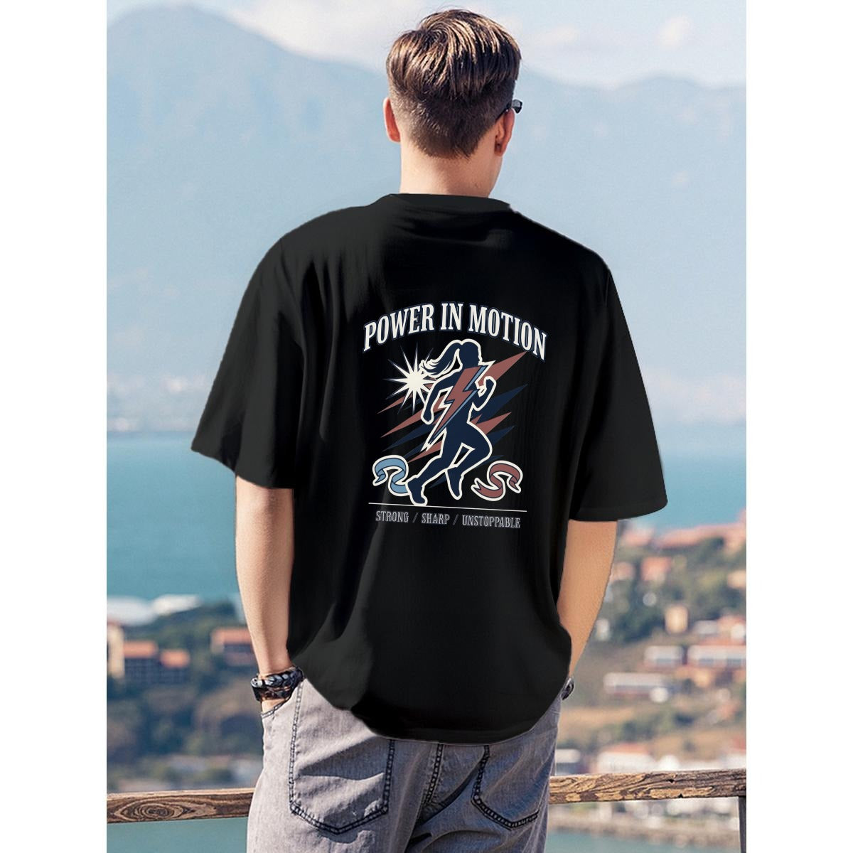 A man viewed from behind wearing a black t-shirt with a large graphic print on the back that reads 'POWER IN MOTION' above an illustration of a runner, set against a scenic coastal background.