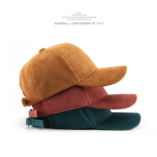 Stack of three corduroy baseball caps in brown, red, and green on a white background.