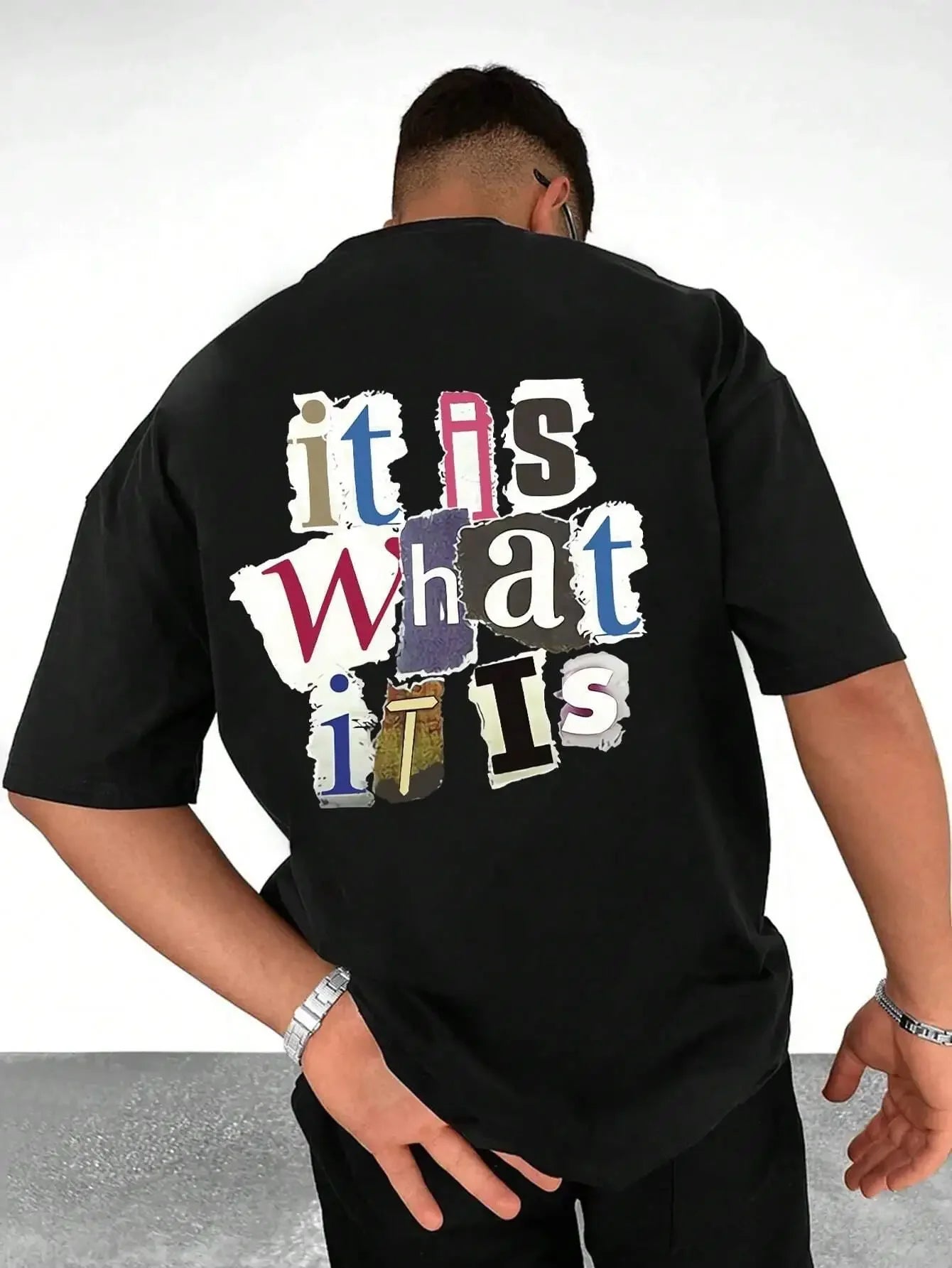 Person wearing a oversized black slogan graphic t-shirt with colorful text design on the back.