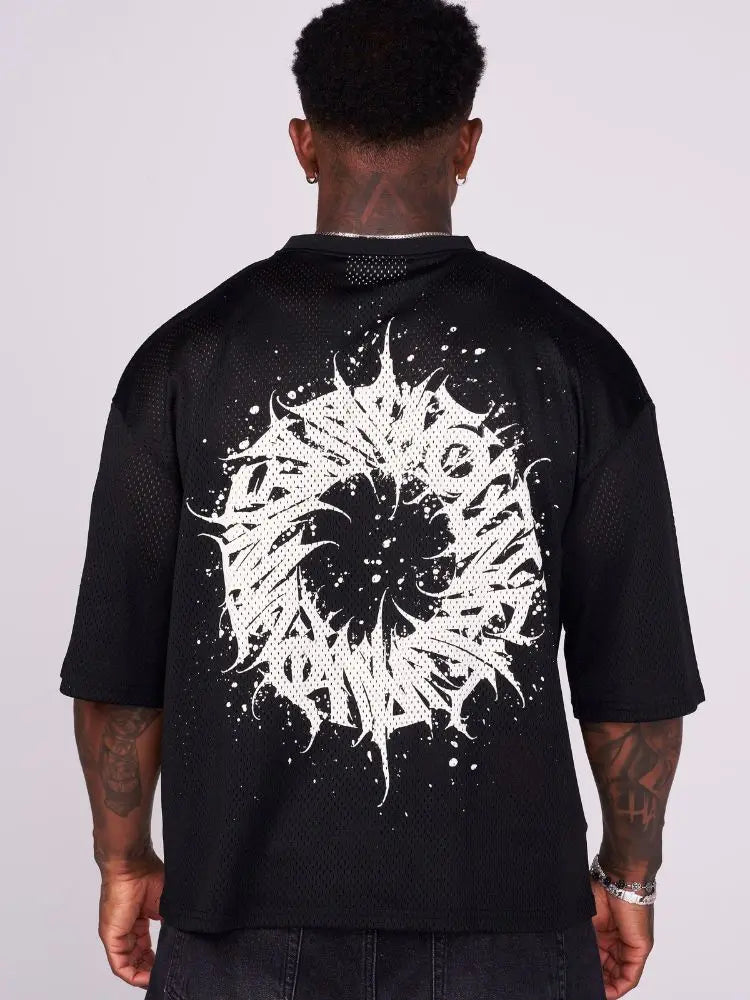 Man wearing an oversized black t shirt graphic with a white maelstrom design on the back against a plain background