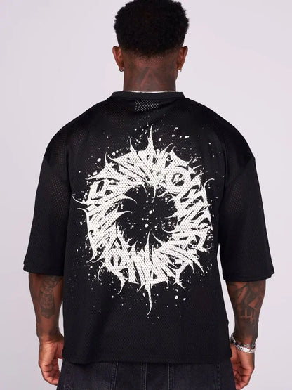 Man wearing an oversized black t shirt graphic with a white maelstrom design on the back against a plain background